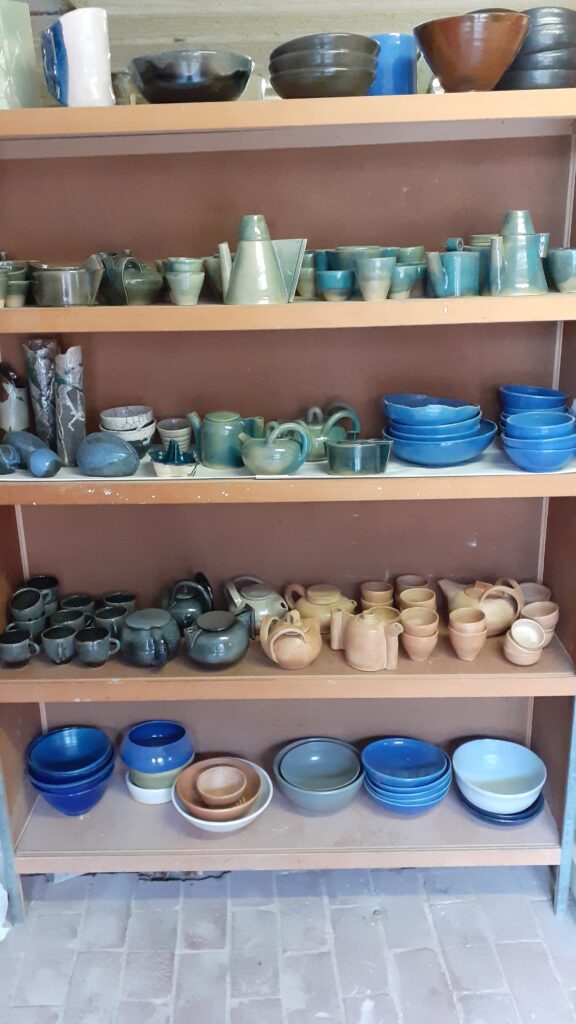 des réalisations de céramique de Bernard : des théières, des tasses et gobelets. Quelques plats et vases sur le haut du présentoirs. Des objets utilitaires et chaque fois des pièces uniques